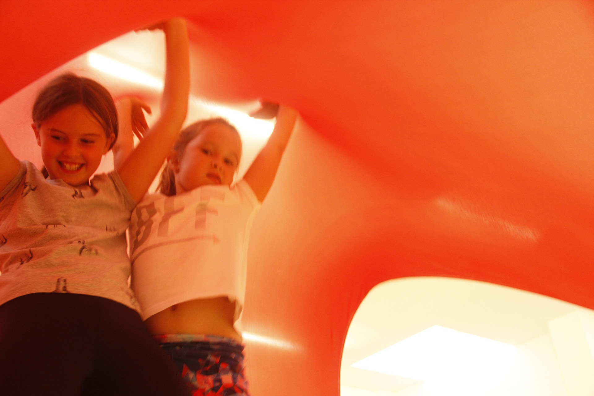 Children underneath a large stretchy Lycra sheet, holding it up as a canopy