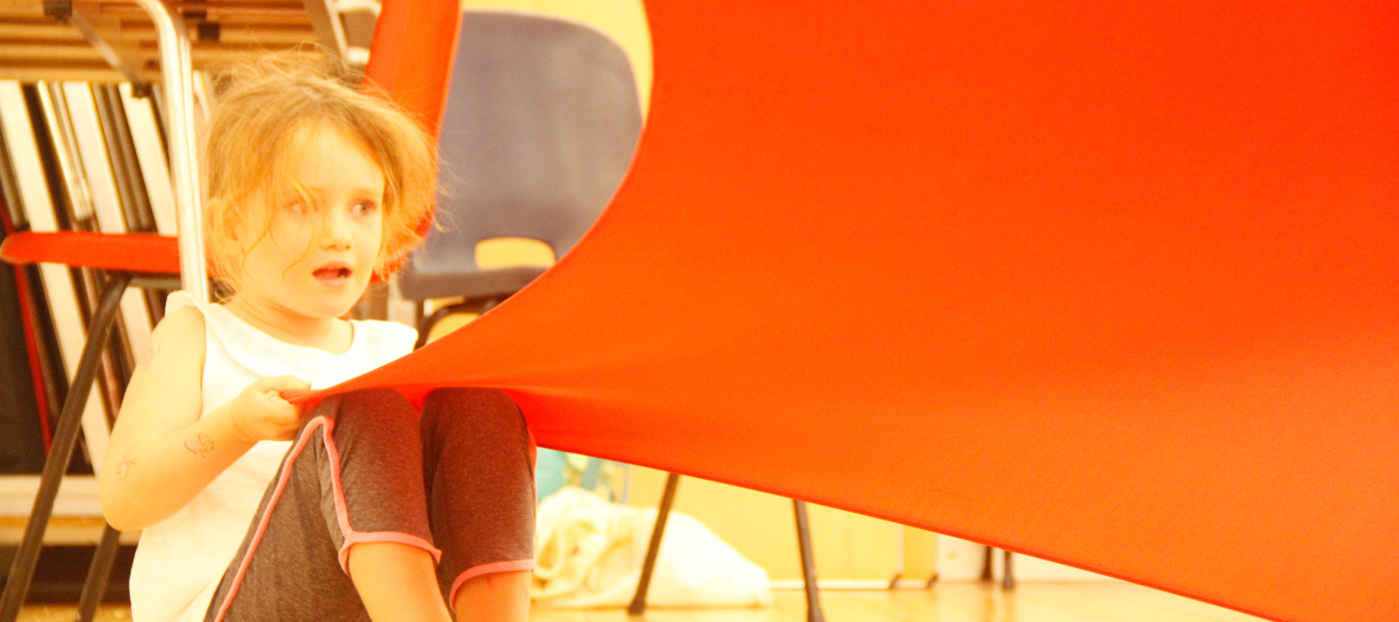 Year 1 pupil creating shapes with a bright red stretch cloth